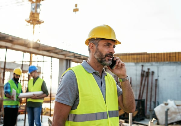 Construction superintendent using a phone to coordinate work and communicate with crews on an active jobsite.