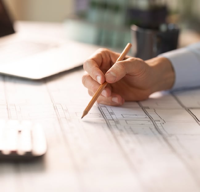 Close-up of contractor workspace with hand drawing on blueprints at desk.