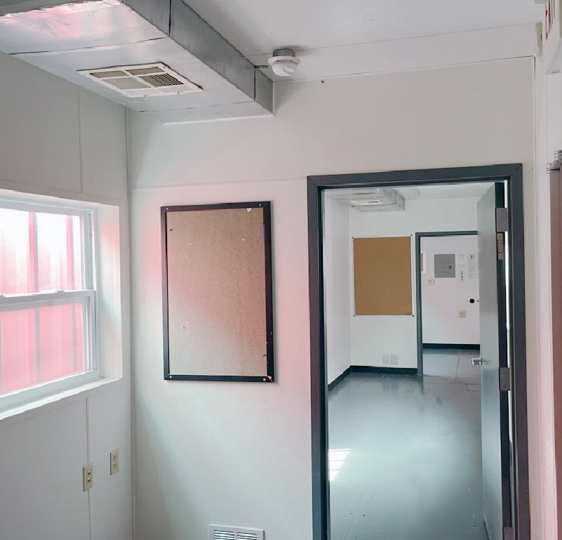 Interior hallway of mobile office with multiple rooms, windows, and bulletin boards.