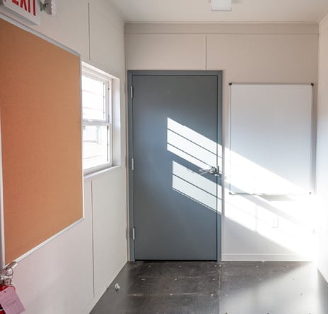 Interior room of portable office with whiteboard, bulletin board, and entry door.