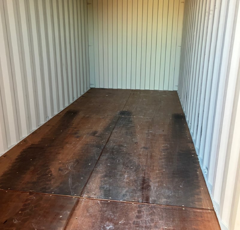 Interior of a used shipping container showing plywood flooring and corrugated steel walls. 